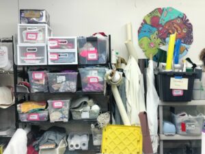 Shelves containing boxes labelled hackable next to bolts of fabric.